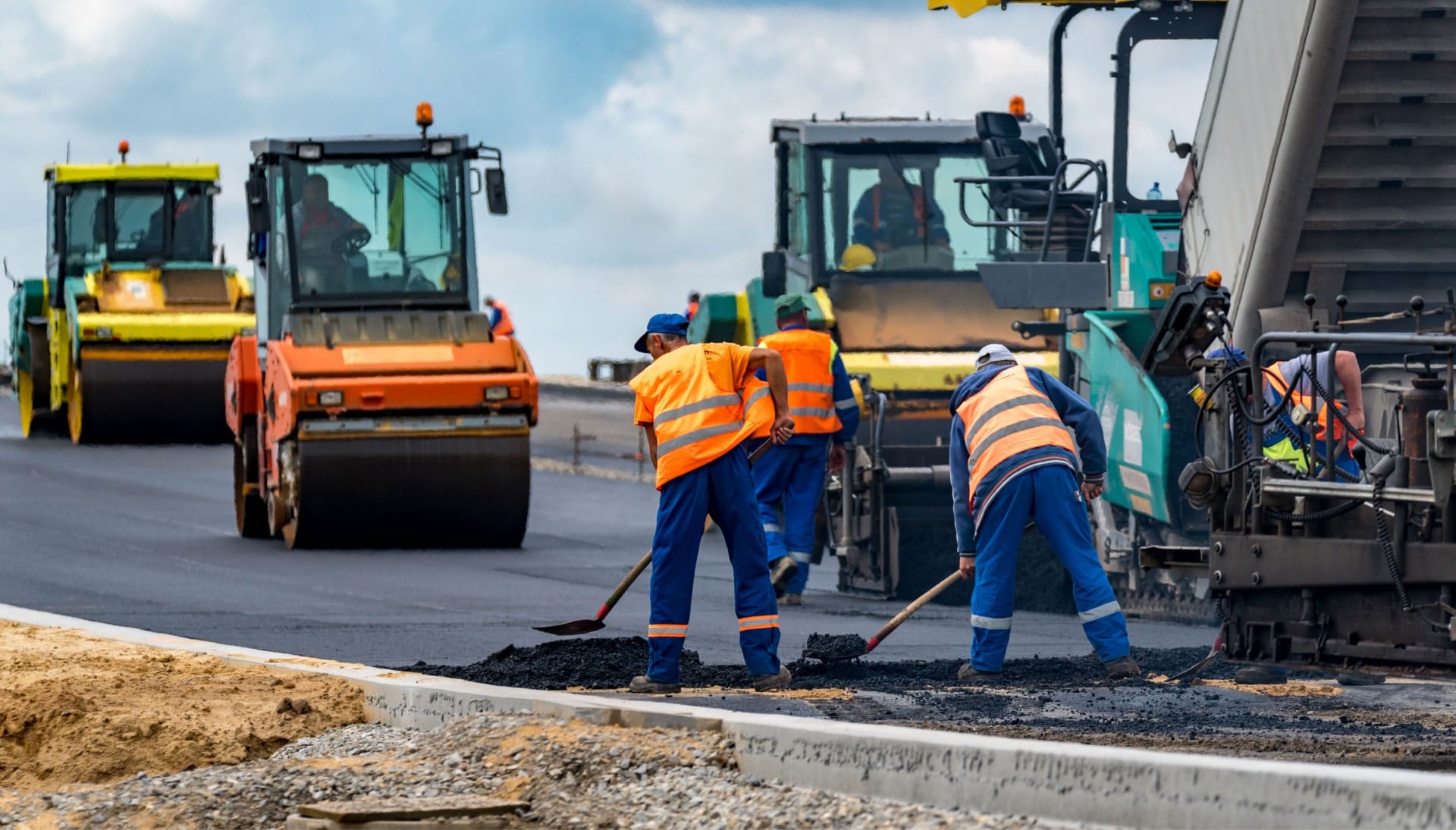 A group of construction workers wearing hard hats and reflective vests, operating heavy machinery and laying down asphalt on a newly excavated road in San Antonio, showcasing the intricate process of building a sturdy and smooth surface.